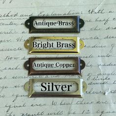 four antique brass and silver name tags sitting on top of a piece of paper with writing