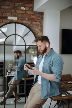 a man sitting on a chair looking at his cell phone while another man stands in the background