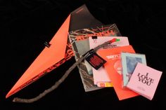 an orange paper airplane sitting on top of a pile of books and other things that are laying around it