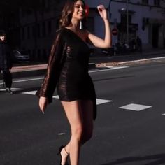 a woman is walking across the street with her hand in her hair and wearing high heels