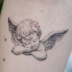 an angel tattoo on the back of a woman's thigh, with her hand resting against her chest