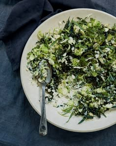 a white plate topped with lots of green vegetables next to a fork and napkin on top of a blue table cloth