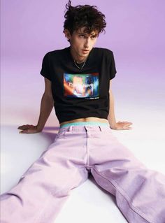 a young man sitting on the ground with his hands in his pockets, wearing purple pants and a black t - shirt