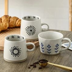 three coffee cups sitting on top of a wooden table next to croissants