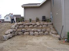 a man standing next to a pile of rocks on top of a dirt field near a house