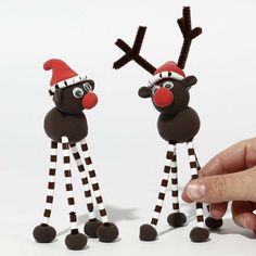 a hand is pointing at two reindeer figurines with santa's hats on