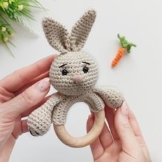 a crocheted bunny holding a wooden ring with carrots on the side and another toy in the background