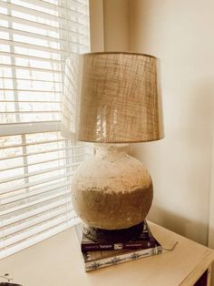 a lamp sitting on top of a wooden table next to a window with blind shades