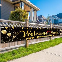 a welcome home banner on a fence in front of a house with balloons and confetti