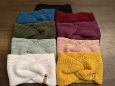 four different colors of knitted headbands sitting on top of a wooden floor