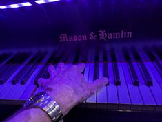 an old man is playing the piano with his hands in front of it and purple lighting behind him