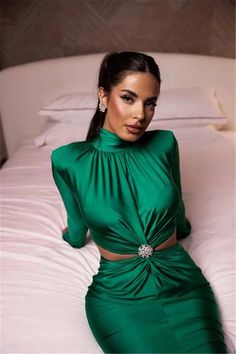 a woman sitting on top of a bed wearing a green dress with high neck and long sleeves