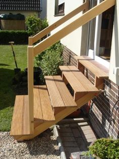 a wooden stair case next to a brick wall and green grass in front of a house