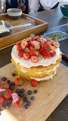 a cake with strawberries and blueberries on top is sitting on a cutting board