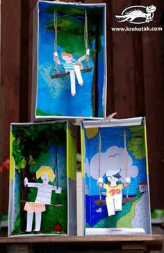 three boxes with paper cut out of people on swings