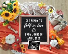 a baby announcement surrounded by flowers, pumpkins and other fall decorations on a table