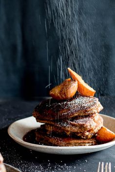 a stack of pancakes with powdered sugar and orange wedges on top, sprinkled with icing