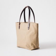 The Field Tan Canvas tote is a canvas and leather tote handmade in the KMM & Co. studio in Atlanta. Each one is meticulously crafted from heavyweight canvas and gorgeous full-grain leather. Field Tan Canvas is a type of cotton canvas known as duck cloth. It's one of the most durable types of cloth, and it's structured enough to stand up on its own. The Field Tan Canvas tote comes standard with Dark Brown handles. Classic Everyday Waxed Canvas Bag, Everyday Classic Canvas Bag With Double Handle, Classic Everyday Canvas Bag With Double Handle, Classic Canvas Bag With Double Handle For Everyday, Everyday Duck Canvas Bag With Leather Trim, Everyday Beige Coated Canvas Bag, Classic Everyday Waxed Canvas Shoulder Bag, Classic Waxed Canvas Everyday Shoulder Bag, Classic Waxed Canvas Shoulder Bag For Everyday