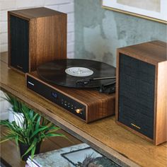 a record player sitting on top of a wooden shelf next to two speakers and a plant