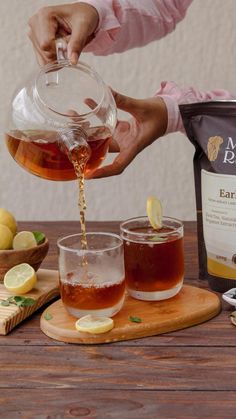 a person pouring tea into two glasses on a wooden table with lemons and honey