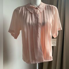 This La Blouse Vintage Top Is A Must-Have For Any Fashion-Forward Woman. The Top Features Short Sleeves And A Collared Neckline With Hidden Buttons. The Blush Pink Color And Pleated Front Make It Perfect For A Variety Of Occasions, Including Travel, Casual Outings, And Workwear. Made Of High-Quality Polyester Fabric, This Blouse Is Both Comfortable And Stylish. It Also Comes With Shoulder Pads And Intricate Embroidered Accents. Whether You're Dressing Up Or Down, This Top Is A Versatile Addition Feminine Peach V-neck Blouse, Pink Feminine V-neck Shirt, Feminine Fitted Peach Blouse, Fitted Feminine Peach Blouse, Feminine Blouse With Collar For Daywear, Feminine Blouse For Daywear, Elegant Peach V-neck Top, Pink Collared Tops For Daywear, Feminine Pink Tops For Daywear