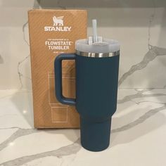 a blue travel mug sitting next to a cardboard box on a marble counter with a straw in it