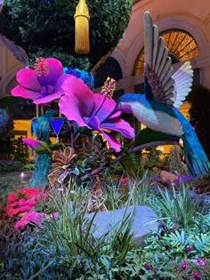 a bird statue sitting on top of a lush green field next to flowers and plants