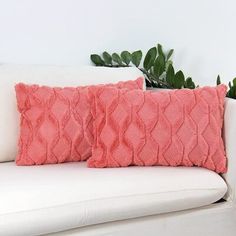 two pink pillows on a white couch next to a potted plant