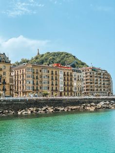 an old building is next to the water in front of some buildings on a hill