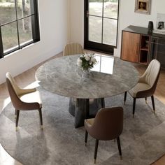 a round table with chairs around it in front of two windows and a rug on the floor