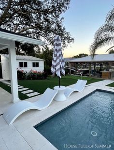 an outdoor swimming pool with lounge chairs and an umbrella next to it in front of a house