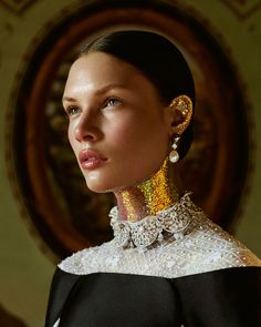 a woman in a black and white dress with gold jewelry on her neck, looking off to the side