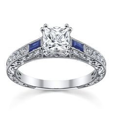 a white gold engagement ring with blue sapphire stones on the sides and a princess cut diamond center