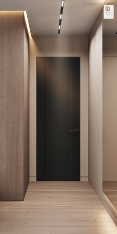 an empty room with a black door and wooden flooring is lit by recessed lights