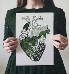 a woman holding up a drawing of a heart with flowers and leaves on it in front of her face