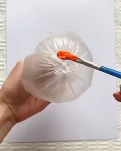 a hand holding a plastic ball with a paintbrush in it and an empty piece of paper behind it