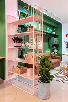 a pink shelf filled with lots of books next to a plant in a vase on top of a tiled floor