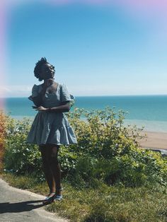 a woman in a dress standing on the side of a road next to the ocean