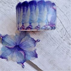 a purple and blue flower sitting on top of a wooden table next to a roll of tape