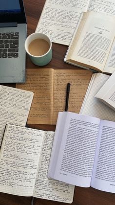 an open book sitting on top of a wooden table next to a laptop and cup of coffee