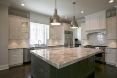 a large kitchen with an island in the middle and two pendant lights hanging from the ceiling