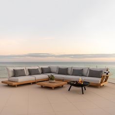 a large sectional couch sitting on top of a wooden table next to the ocean with an open fire pit