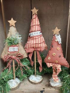 three small christmas trees are on display in front of a wooden wall and decorated with burlap