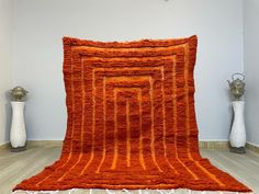 an orange rug is on the floor next to two white vases and a lamp