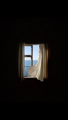 an open window in a dark room overlooking the ocean