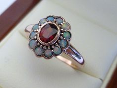 This gorgeous Vintage Inspired Flower Ring has been crafted from 9ct Solid Rose Gold with an oxidised background vintage effect. A bezel set oval cut NATURAL Garnet with surrounding NATURAL Opals brings this ring to life. Notice the stamens that surround the petals of this beautiful ring. This is an elegant Victorian inspired ring which simply looks beautiful on a lady who enjoys wearing fine jewellery from a Vintage era.  THIS VINTAGE INSPIRED GARNET & OPAL RING IS TRULY AN EXQUISITE FINE JEWEL Opal Ring Vintage, Garnet Ring, Funky Jewelry, Garnet Rings, Opal Ring, Multi Stone Ring, Dream Jewelry, Ring Vintage, Ready Made