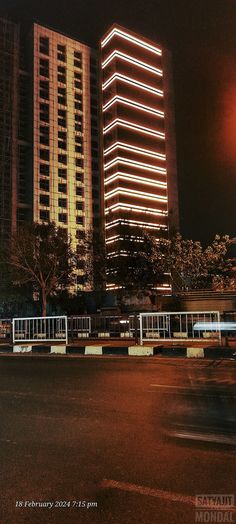 an empty street in front of two tall buildings at night with the lights turned on