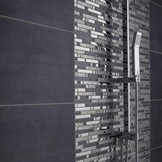 a black and white photo of a shower head in a tiled bathroom with dark walls