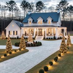 a large white house with christmas lights on the front yard and trees in the driveway