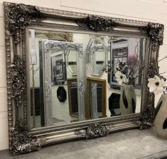 an ornate silver framed mirror sitting on top of a mantle next to a vase with flowers